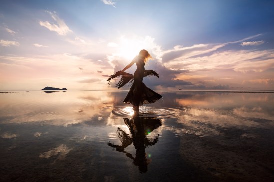Elegant woman dancing on water. Sunset and silhouette.